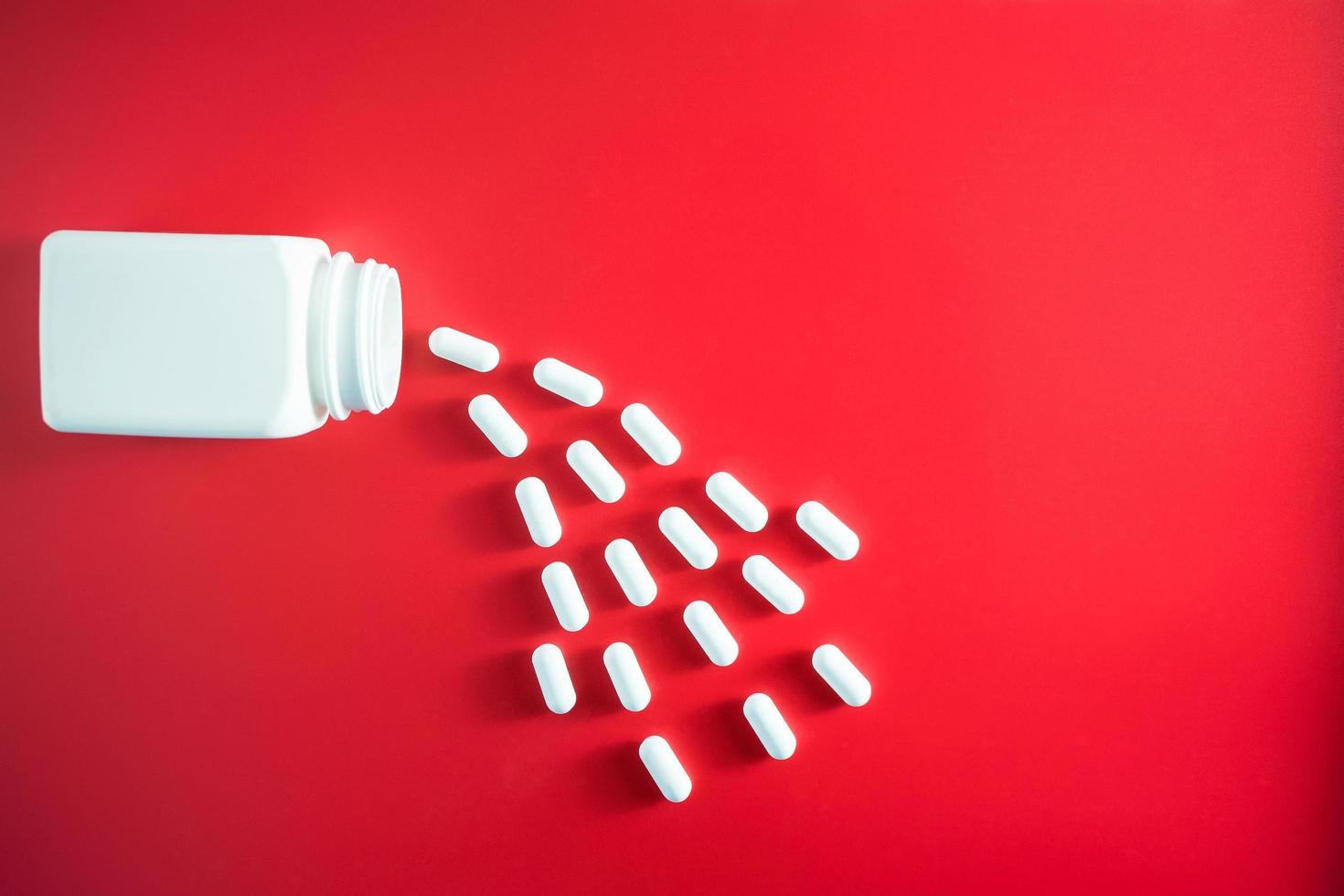 Pillen die uit pillenfles morsen en op rood worden geïsoleerd foto