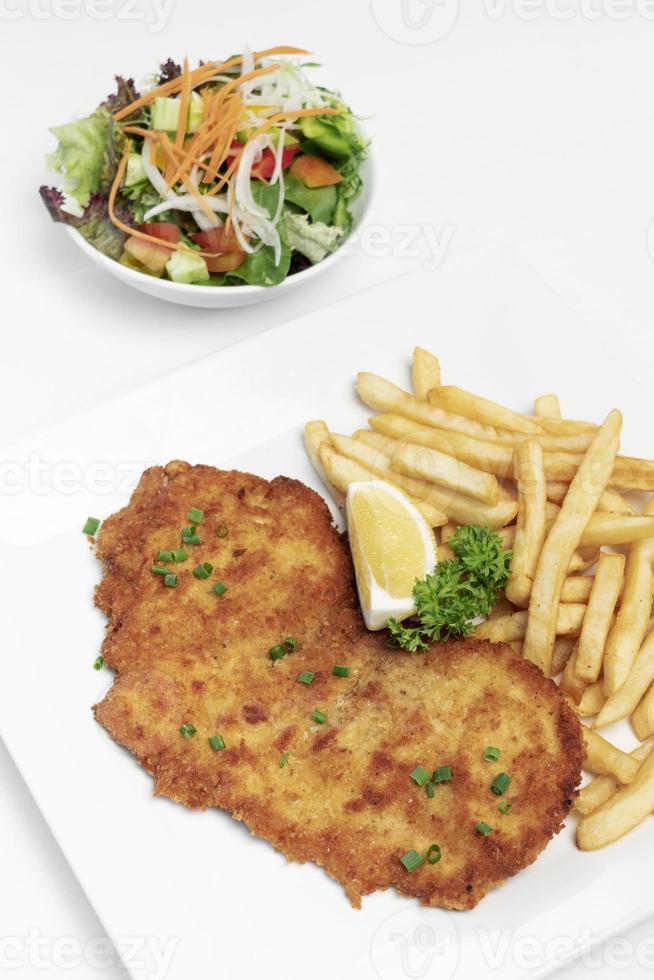 Duits-gepaneerde varkensschnitzel met frietjes op witte studioachtergrond foto