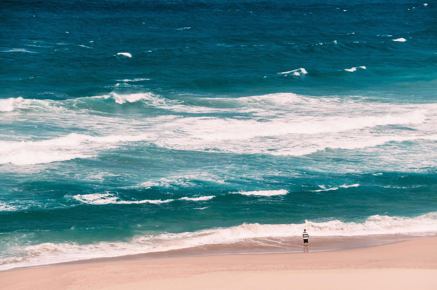 oceaanstrand met grote golven, een visser die staat met een hengel foto