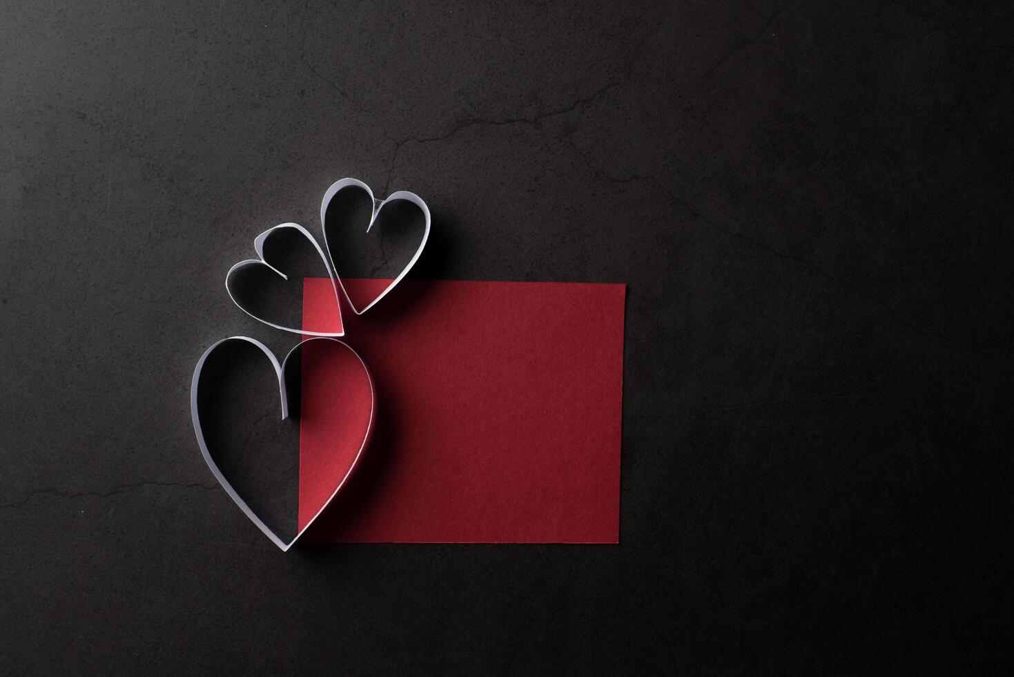 wit hartvormig papier in schaduw rode notitiekaart op zwarte achtergrond. foto