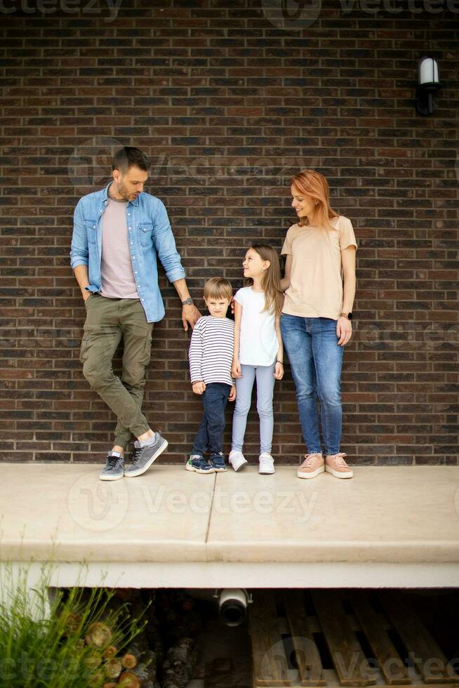 familie met een moeder, vader, zoon en dochter staand door de muur van steen huis foto