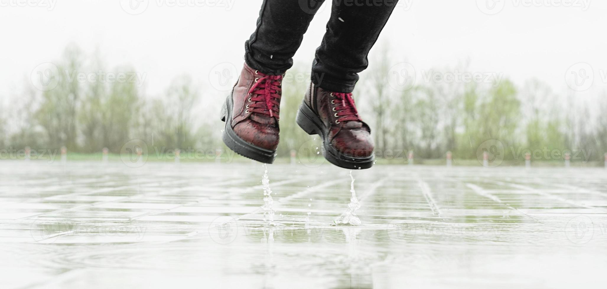 vrouw die in de regen speelt, in plassen springt met spatten foto