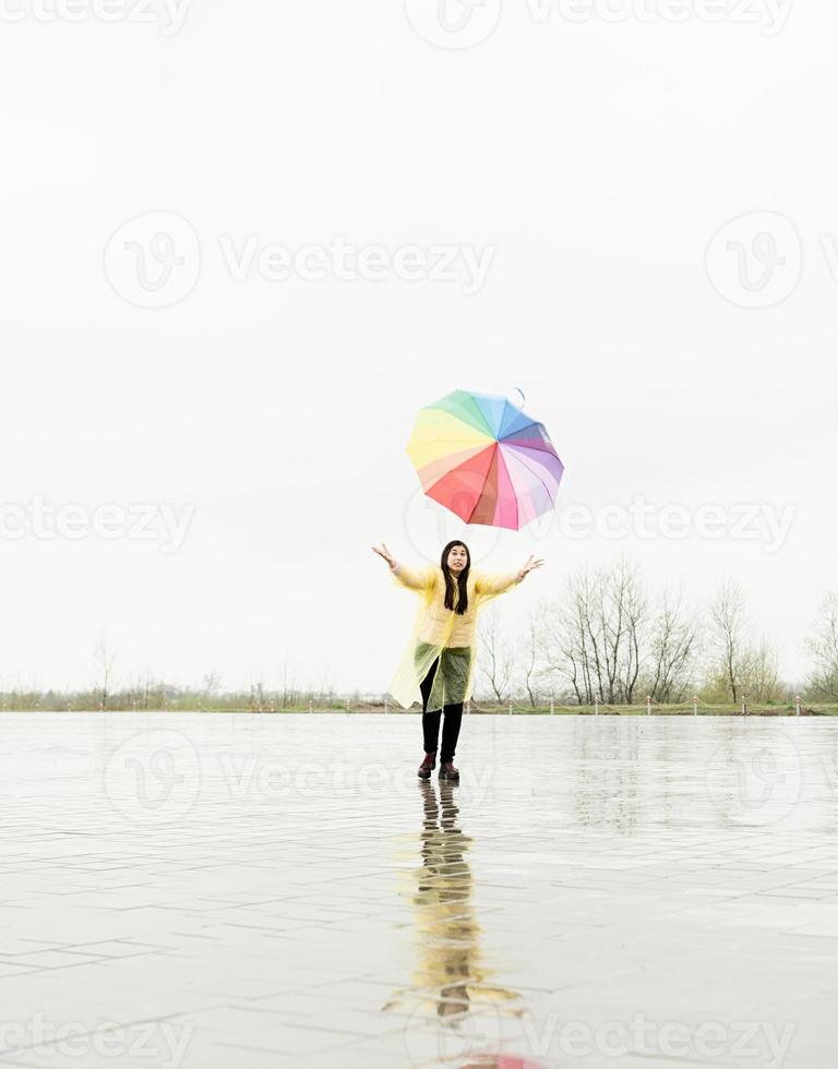 grappige vrouw die kleurrijke paraplu buiten in de regen vangt foto