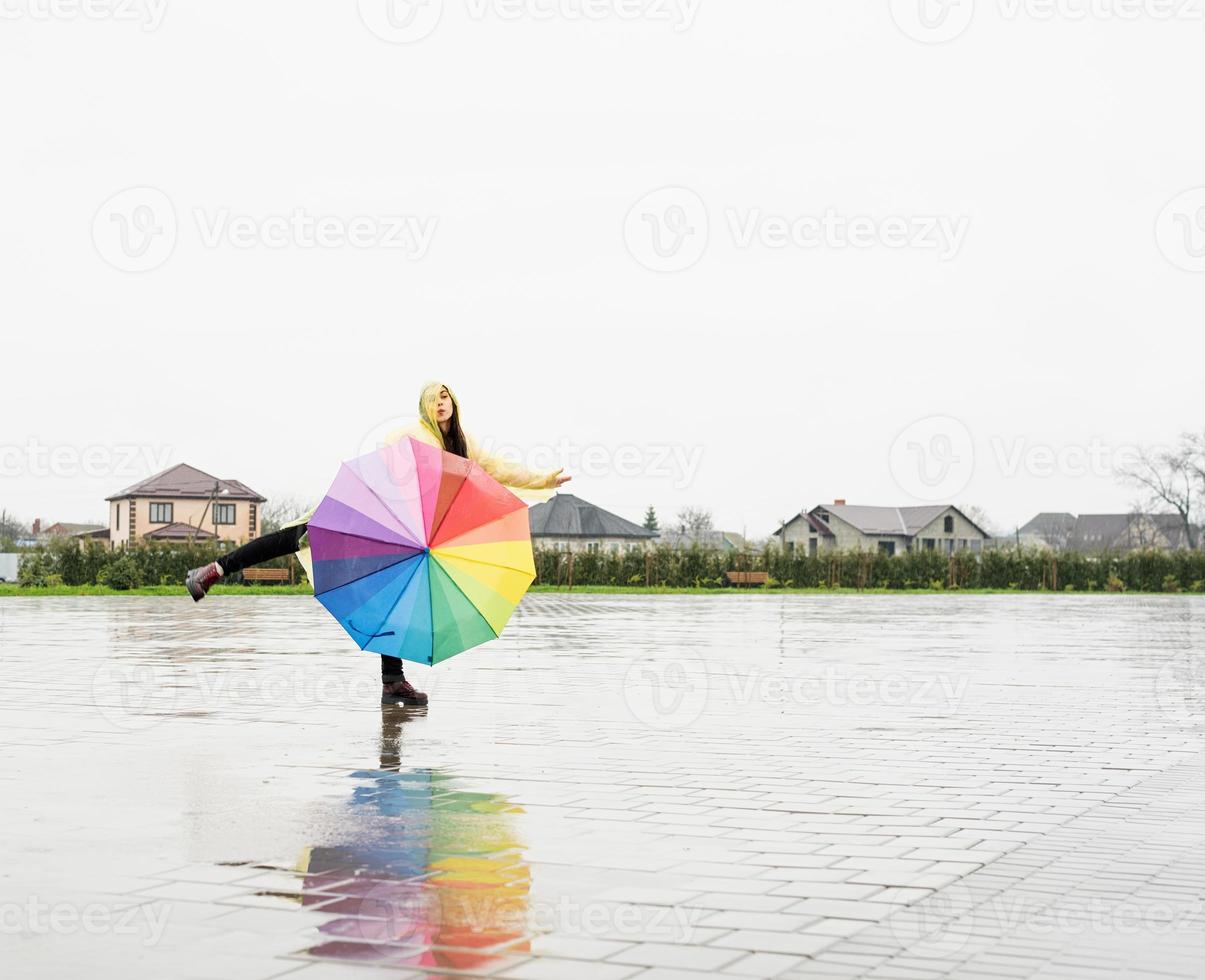 mooie donkerbruine vrouw die kleurrijke paraplu houdt die in de regen danst foto