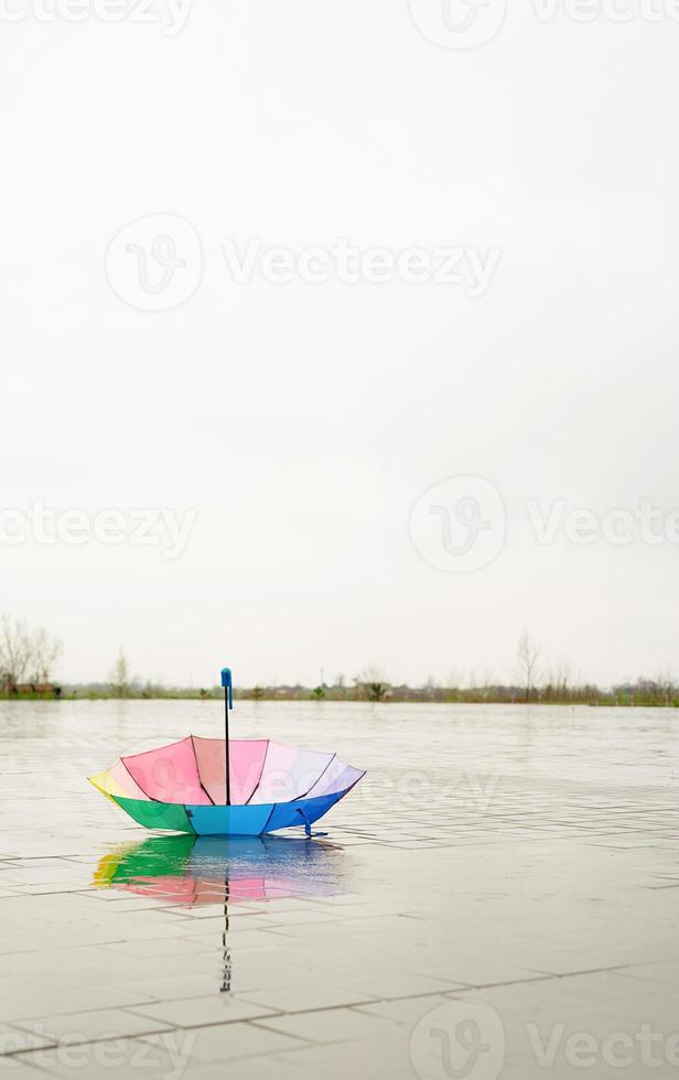 regenboogkleurige paraplu liggend in plassen op de natte straatgrond foto