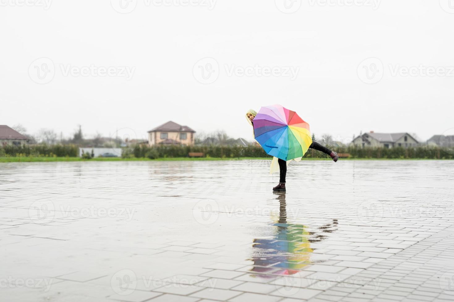 mooie donkerbruine vrouw die kleurrijke paraplu houdt die in de regen danst foto