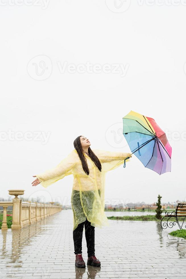 donkerbruine vrouw die kleurrijke paraplu houdt die in de regendruppels vangt foto