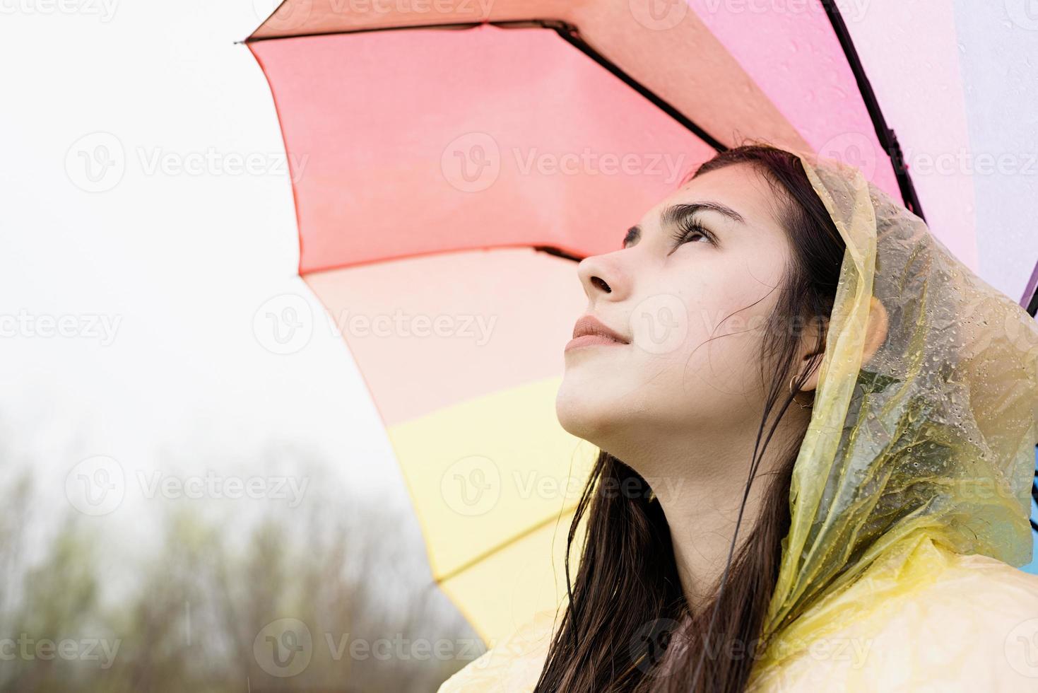 staande vrouw met een regenboogkleurige paraplu, wegkijkend foto