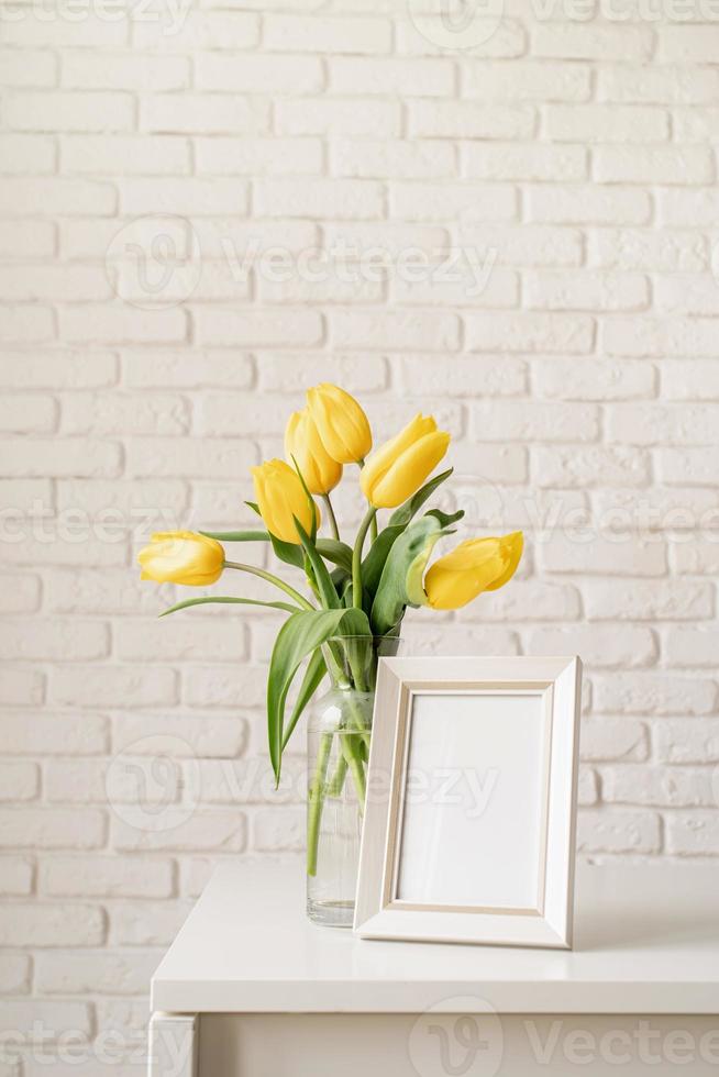 gele tulpen in een glazen vaas en blanco fotolijst foto