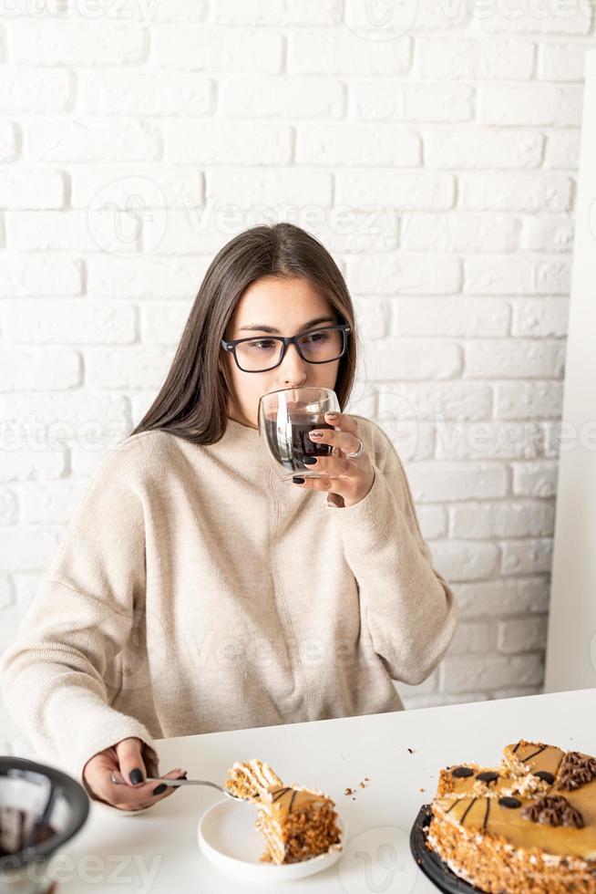 vrouw die aan de witte tafel zit, cake eet en koffie drinkt foto