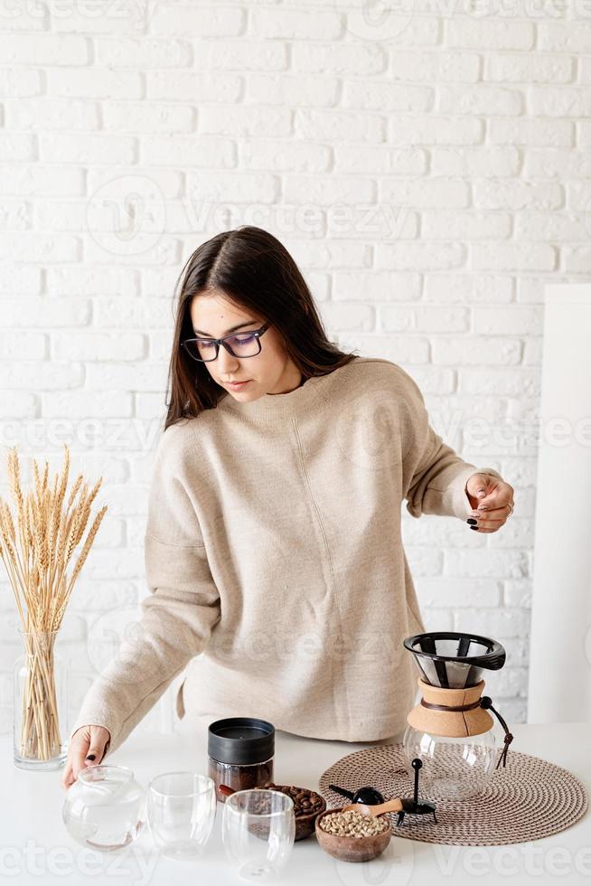 vrouw zet koffie in koffiepot en giet heet water in het filter foto