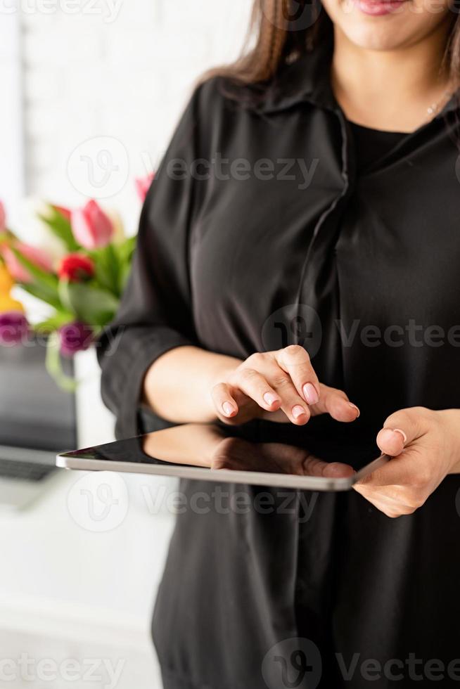 vrouw die aan digitale tablet werkt, emmer verse tulpen op achtergrond foto