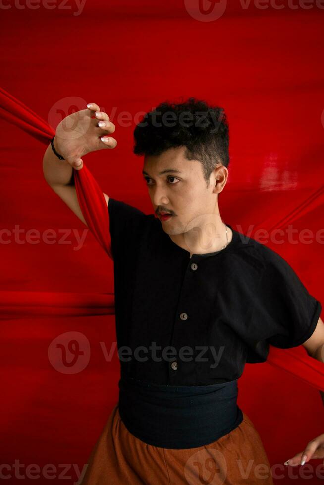 een Aziatisch Mens Holding een rood kleding in zijn armen met een stoutmoedig uitdrukking tegen een rood achtergrond foto