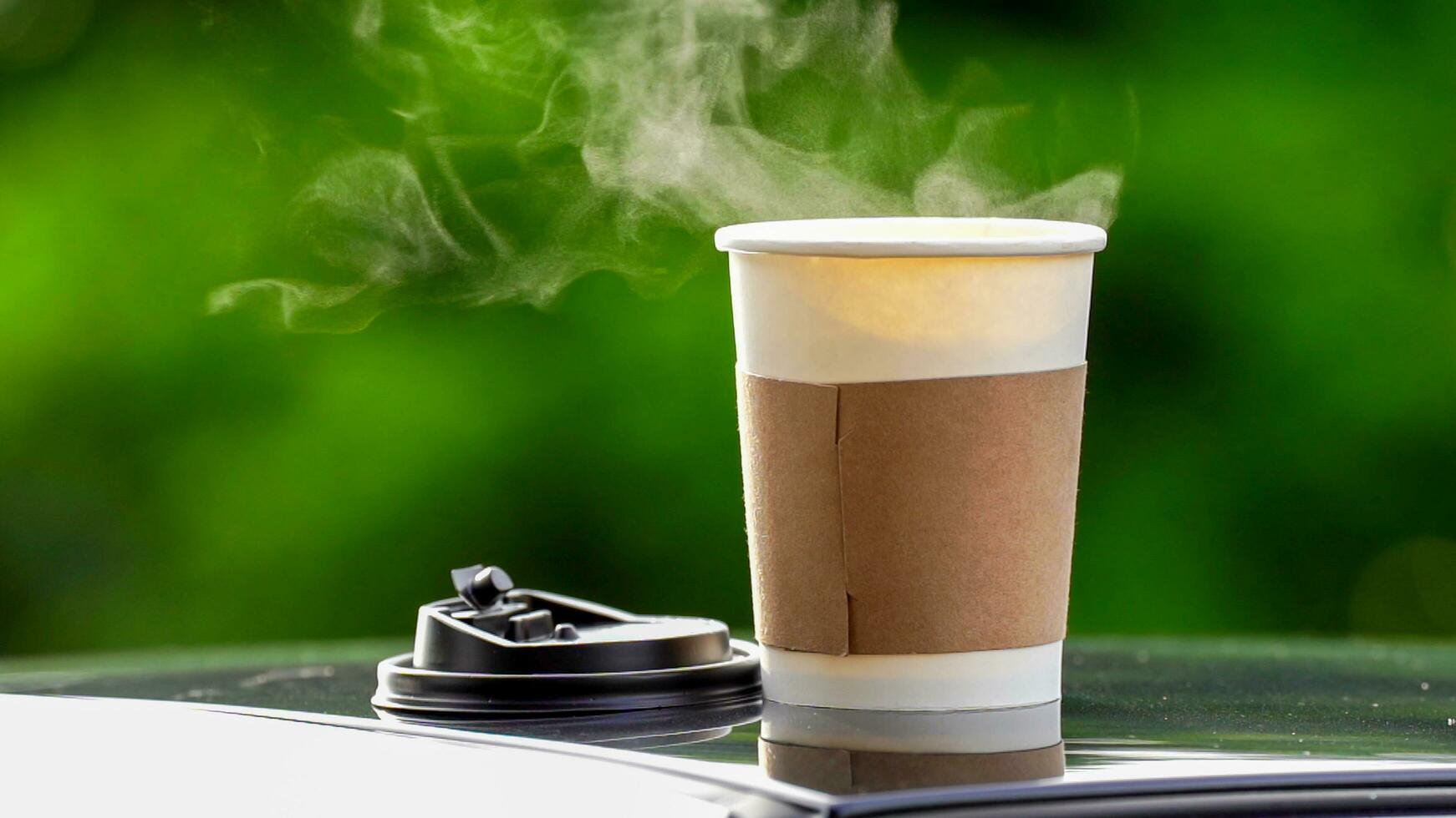 koffie meenemen in een papier kop Aan top van de auto dak groen boom achtergrond Bij zonsopkomst in de ochtend, selectief focus, zacht focus. foto