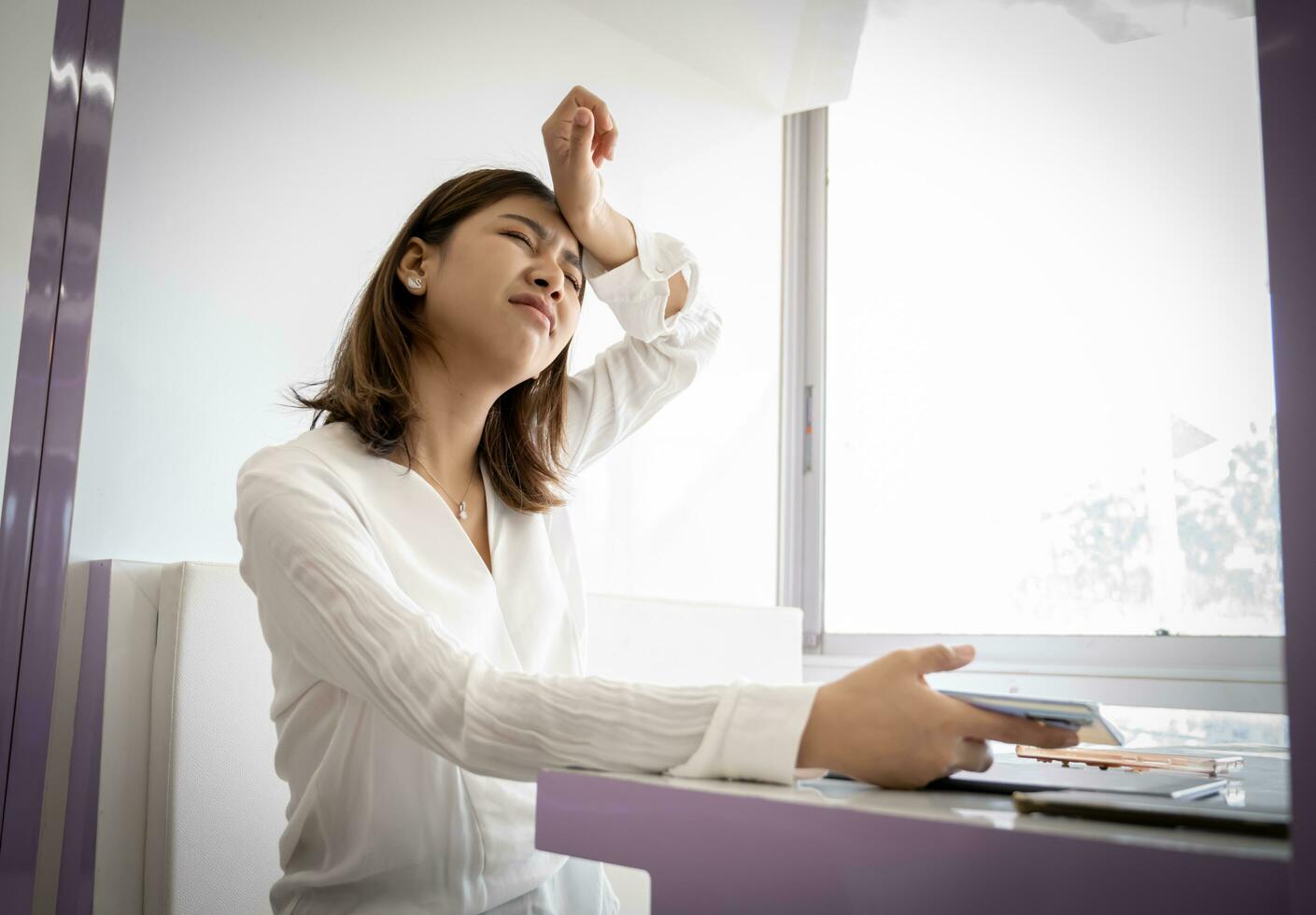 mooi Aziatisch zakenvrouw in dichtbij omhoog schot is ten einde raad voor een baan ze gemist terwijl Holding haar telefoon Aan haar kantoor bureau. foto