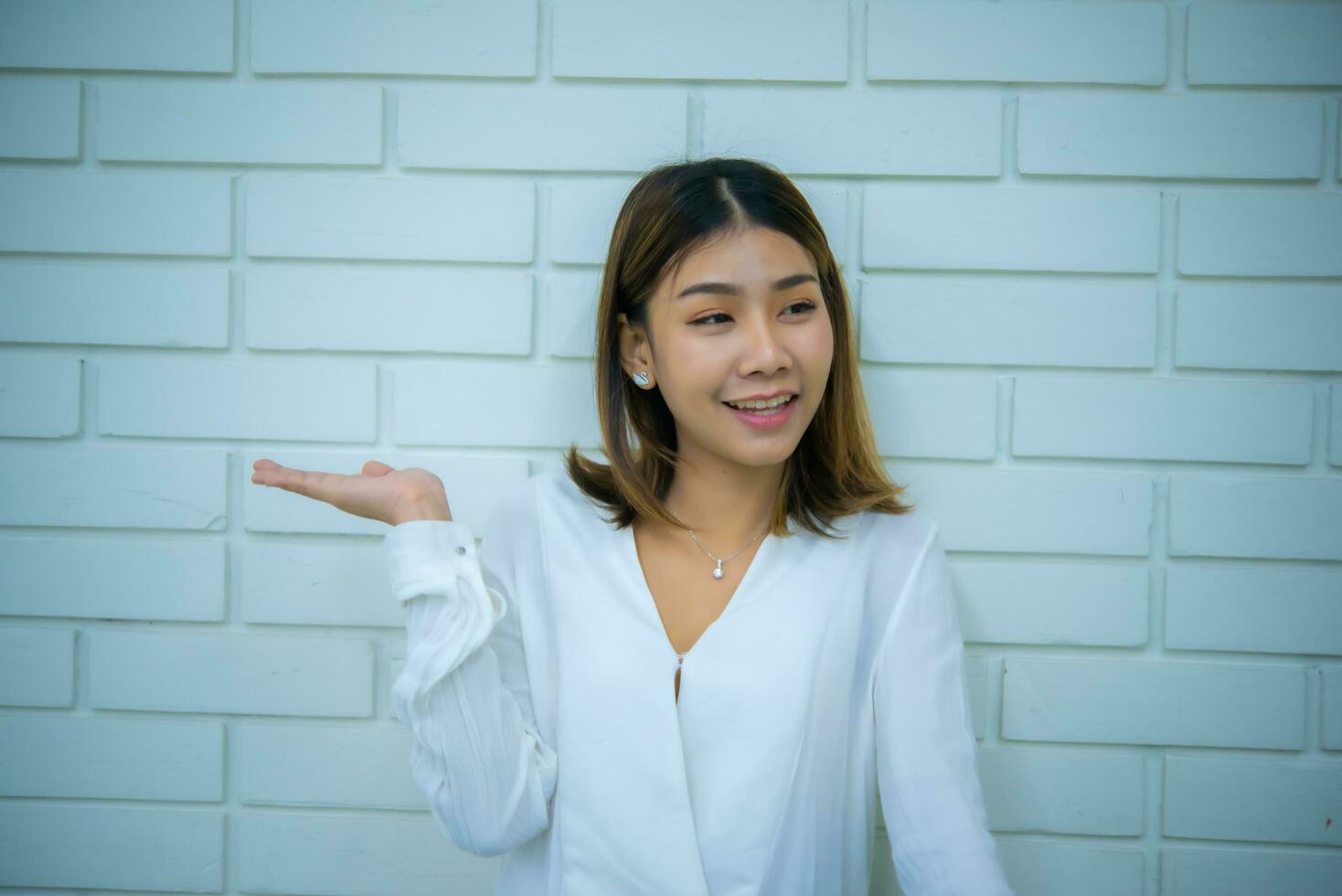 mooi Aziatisch bedrijf vrouw staand met een hand- Uitgang Bij kopiëren Oppervlakte met een glimlach tegen een wit steen achtergrond, digitaal marketing. foto