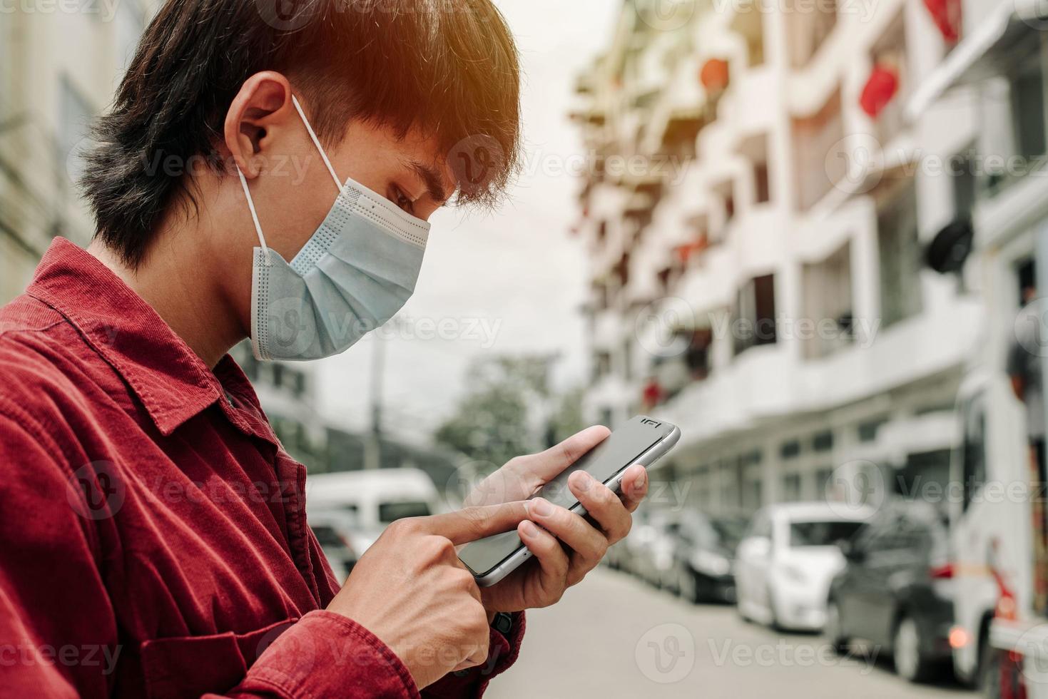 man met medisch gezichtsmasker die de telefoon gebruikt om naar nieuws te zoeken. foto