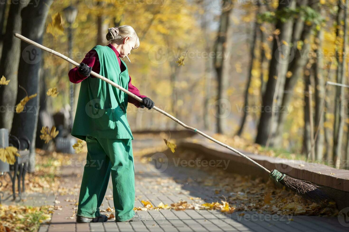 een arbeider reinigt de straat met een bezem. een conciërge reinigt de weg van gedaald bladeren in de val. nut arbeider met bezem schoonmaak foto