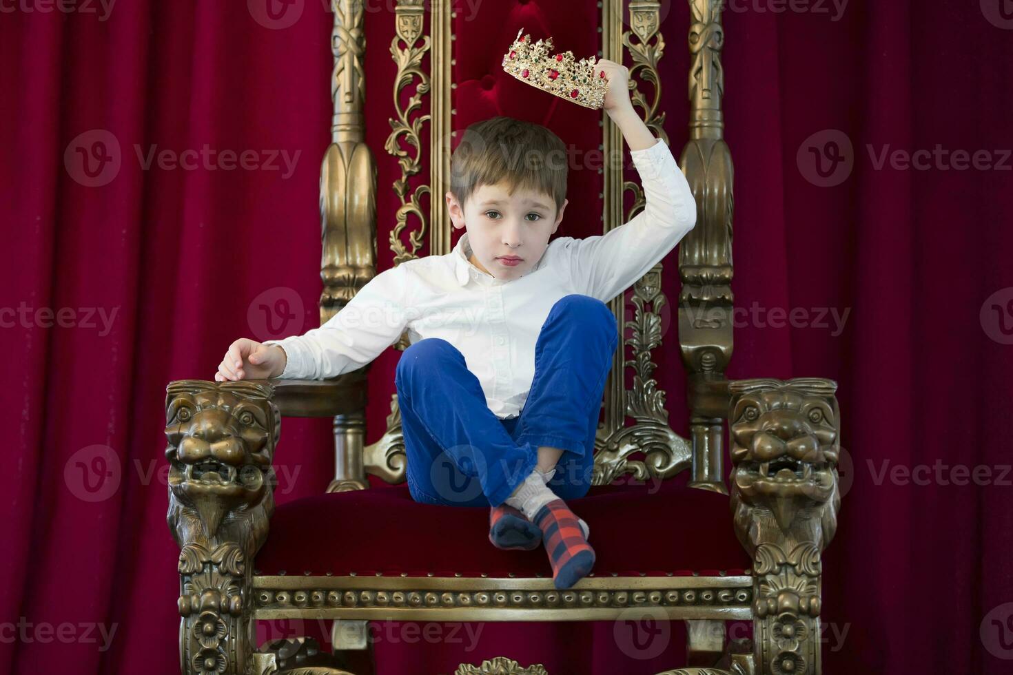 weinig jongen in een kroon in een luxueus stoel.jurk omhoog de kroon foto