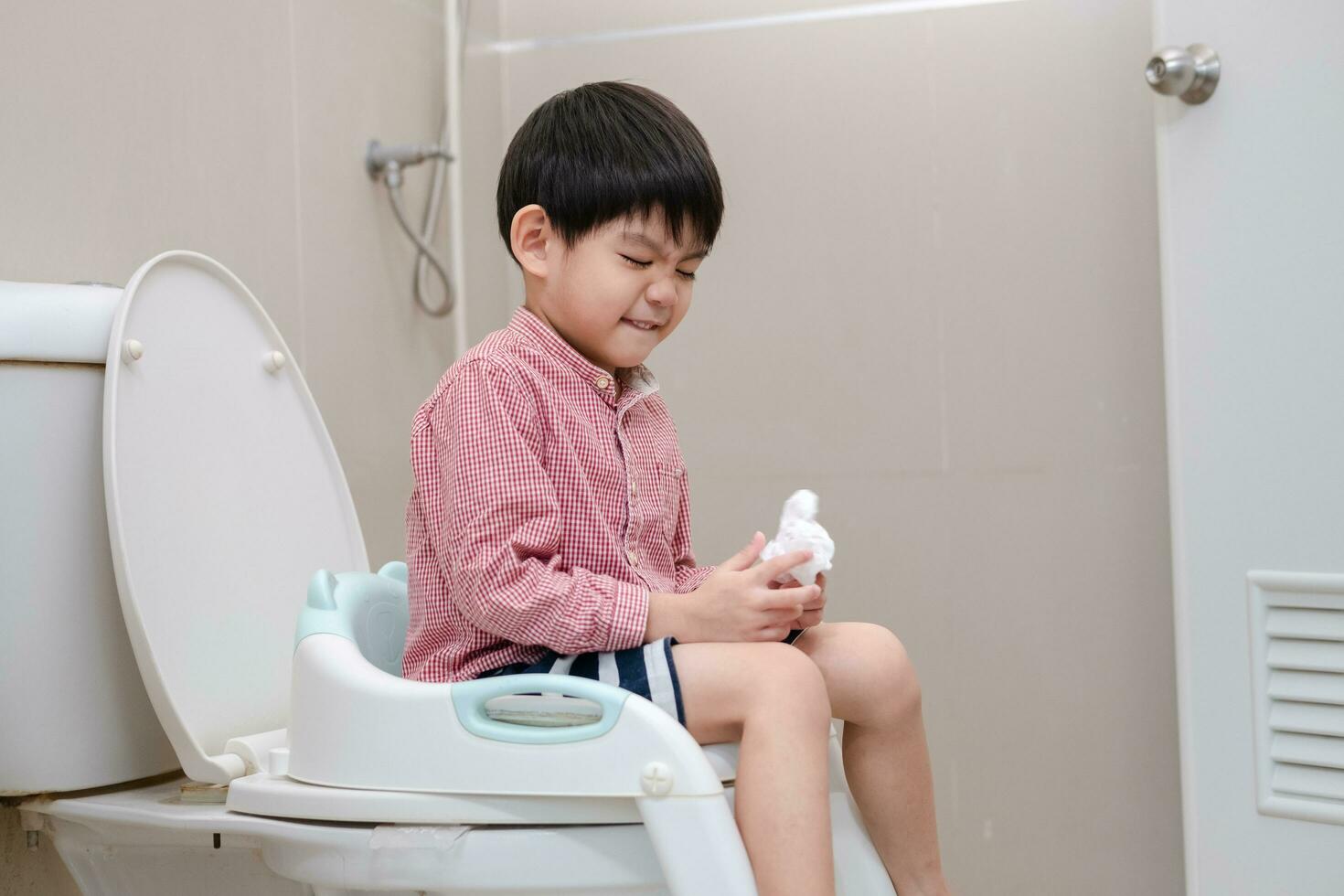 Aziatisch jongen zittend Aan de toilet kom in hand- Holding zakdoek foto