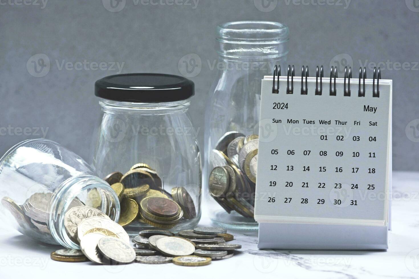 mei 2024 kalender en glas potten met meerdere valuta munten. 2024 financiën concept. foto