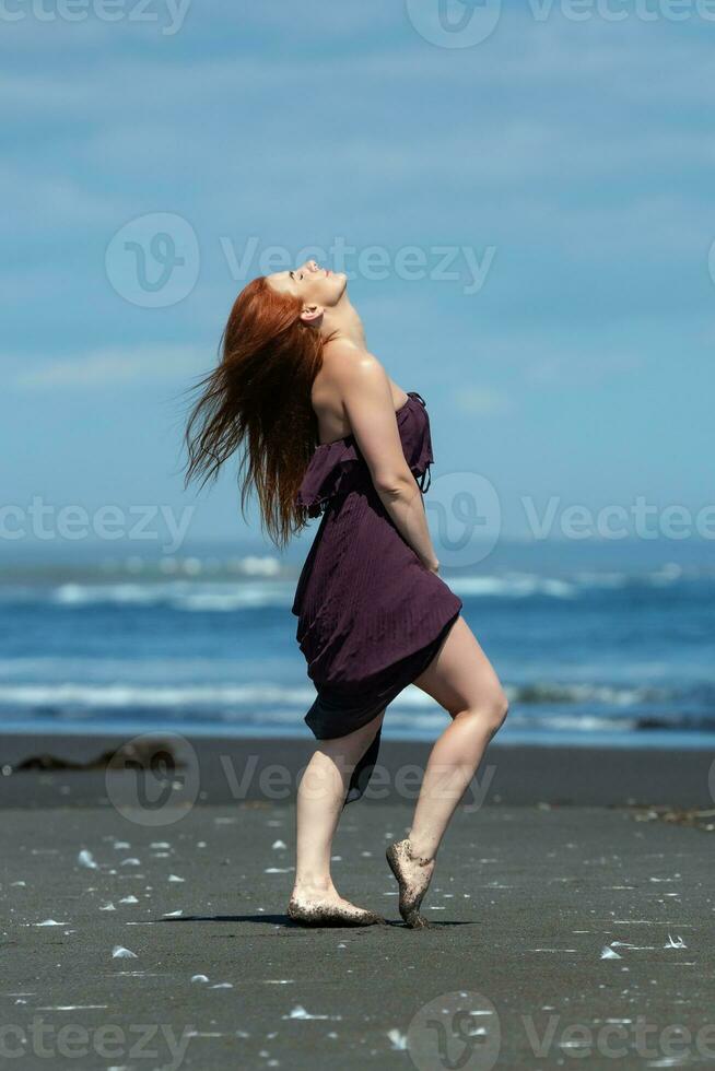 vrouw in lang jurk staand Aan zanderig strand met hoofd op zoek naar boven en ogen gesloten, zonnen foto