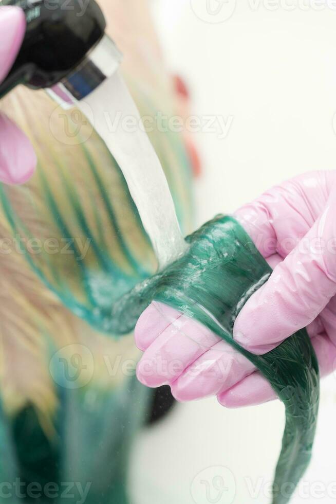 kapper houdt slot haar- in hand- terwijl het wassen haar- van cliënt in douche in wasbak. schoonheid salon, werken professioneel kapper in roze handschoenen foto