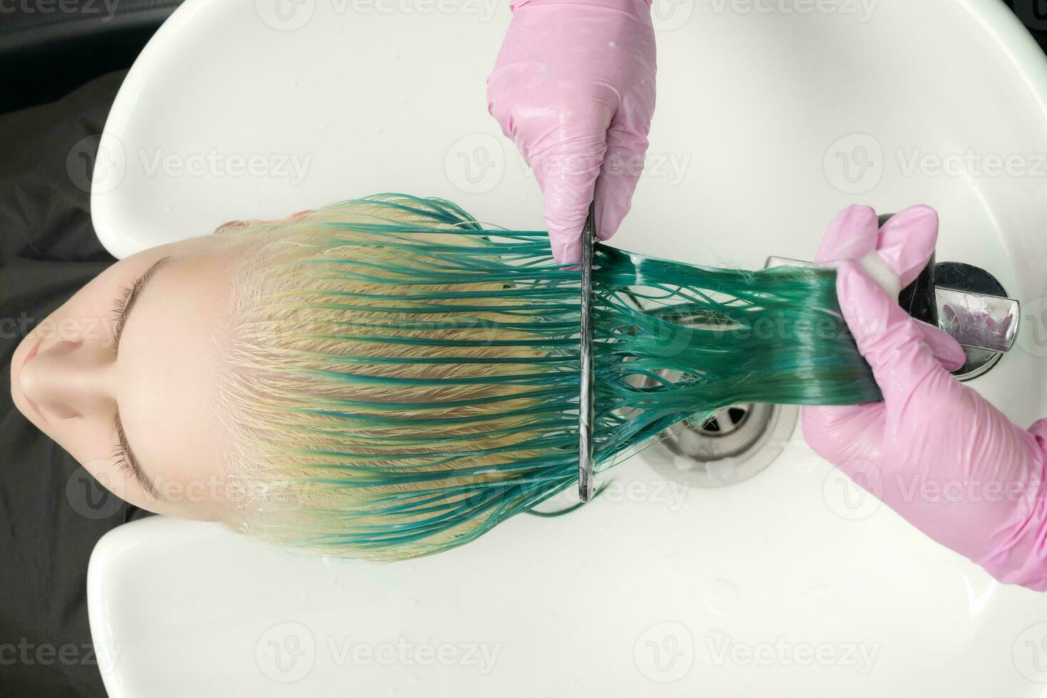 top visie van kapper in beschermend handschoen houdt haar- in hand- en kammen lang groen en verkleurd haar- van klant terwijl het wassen haar- in douche foto