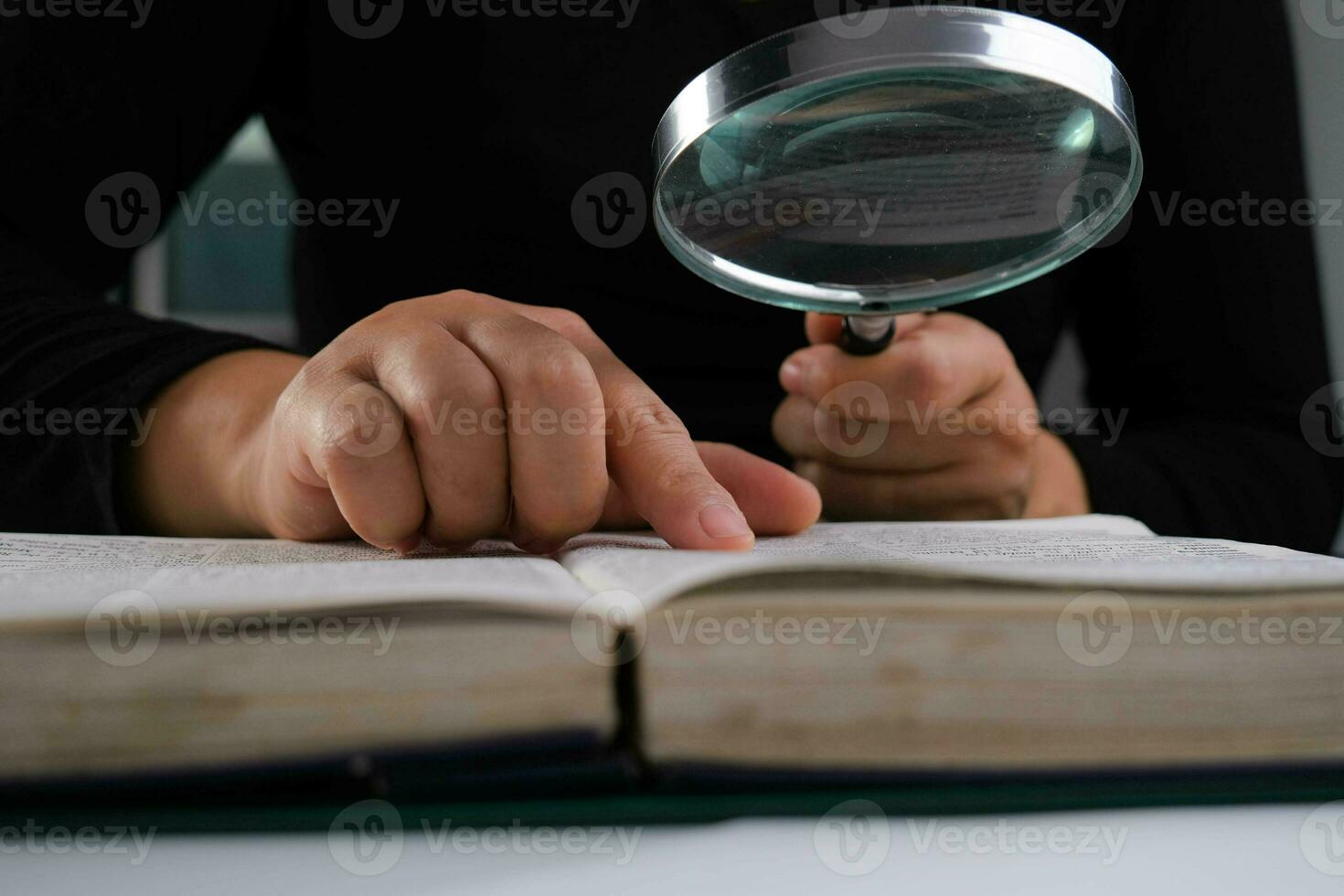 detailopname van een vrouw op zoek door een vergroten glas Bij een leerboek. vergroten glas in hand- en Open boek Aan tafel. onderwijs en Onderzoek concept. foto