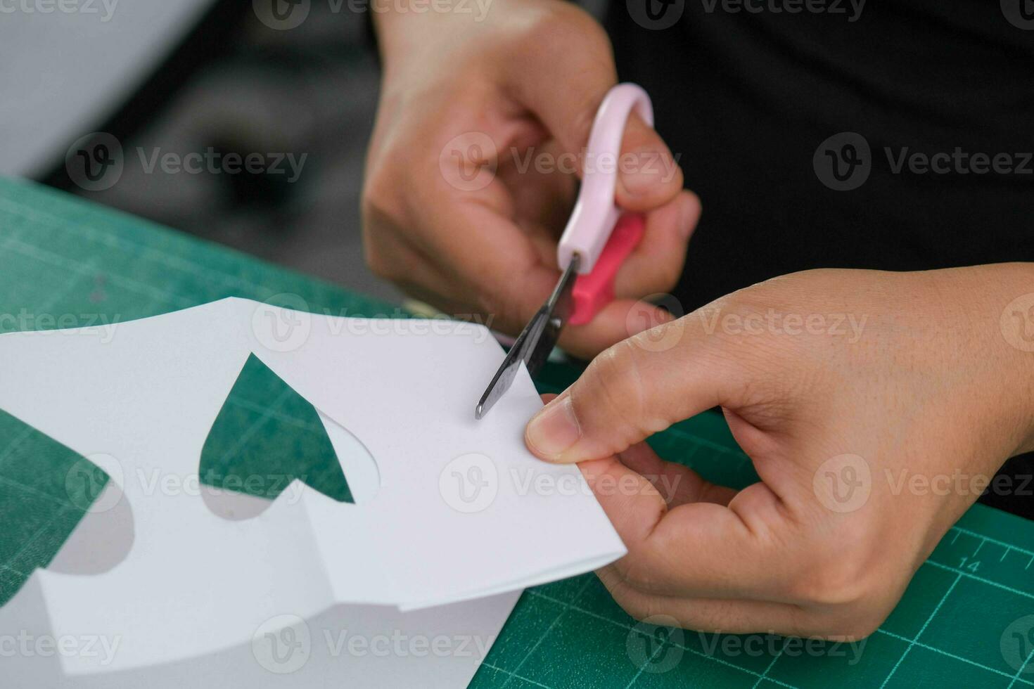 een vrouw bezuinigingen uit een wit hartvormig papier met schaar naar versieren. Valentijnsdag dag groet kaart of vakantie geschenk concept. foto