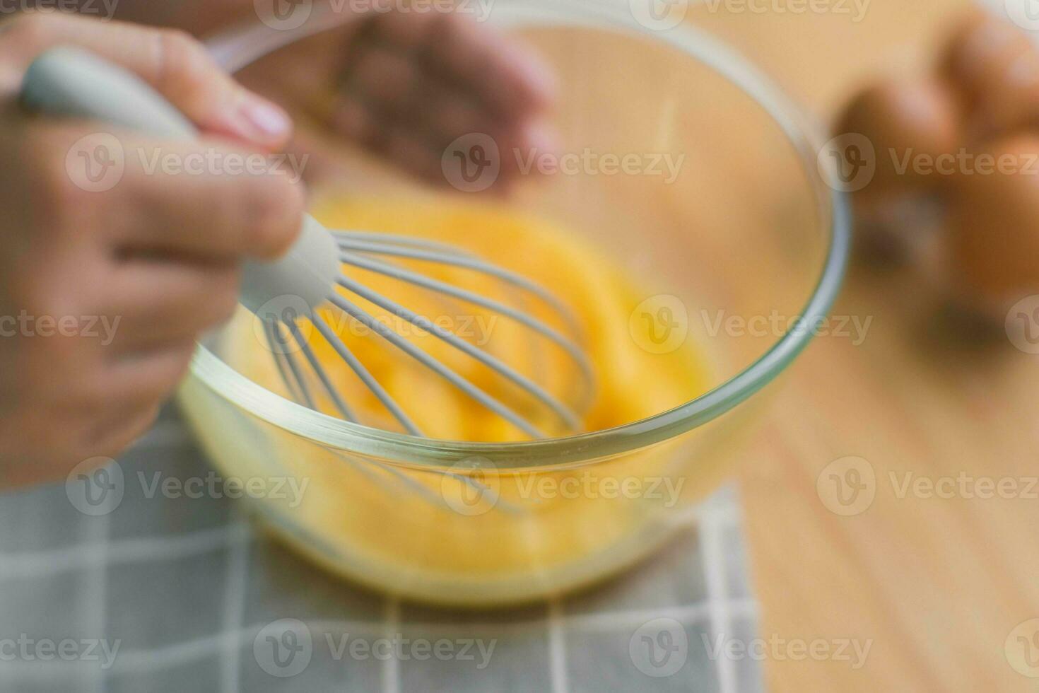 jong vrouw Koken in helder keuken, handen kloppen eieren in een kom geplaatst Aan handdoek en houten tafel. voorbereidingen treffen ingrediënten voor gezond Koken. eigengemaakt voedsel foto