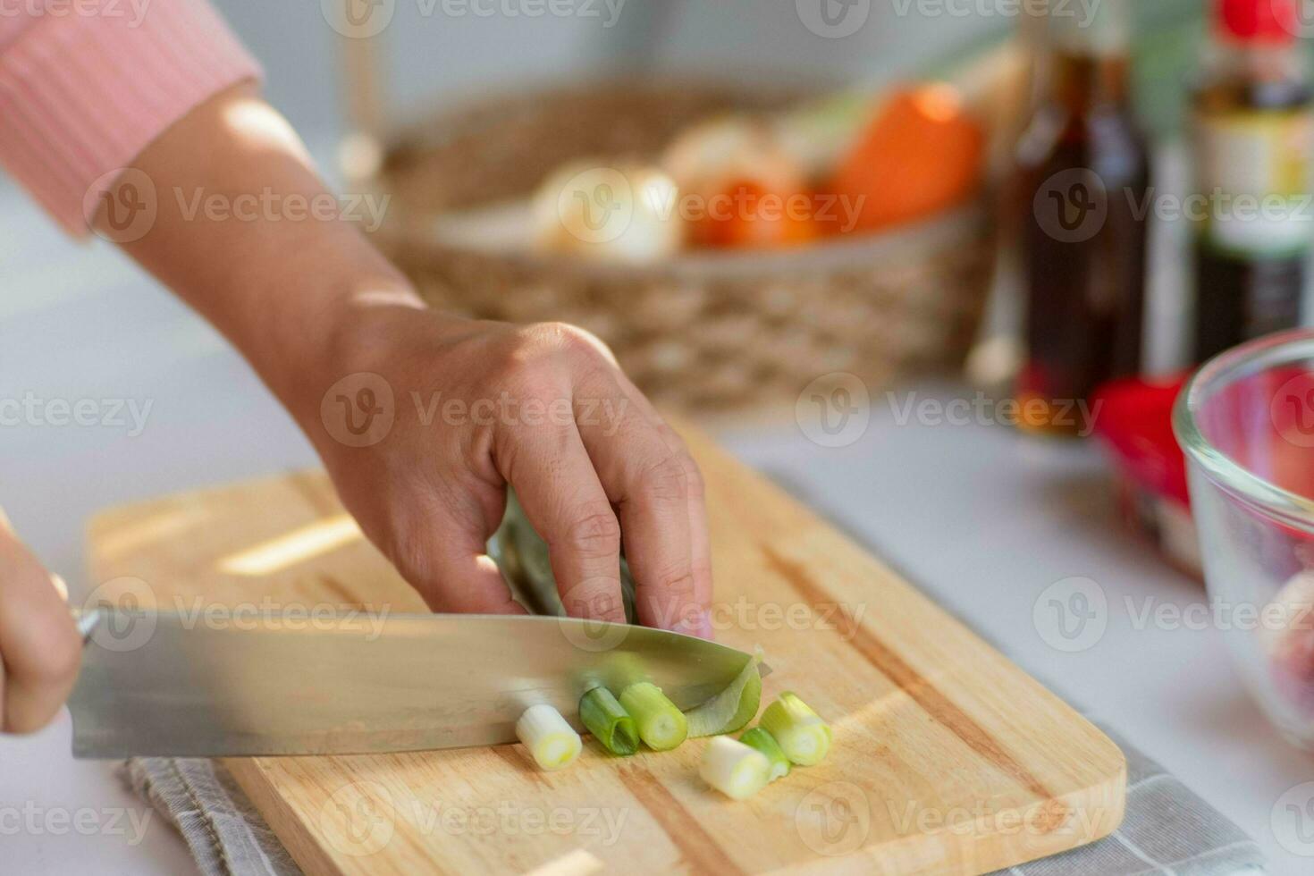 vrouw hand- gebruik makend van een mes naar besnoeiing negi Japans lang ui of Japans lente-ui of groen ui Aan houten snijdend bord. vrouw voorbereidingen treffen voedsel in de keuken Bij huis. foto