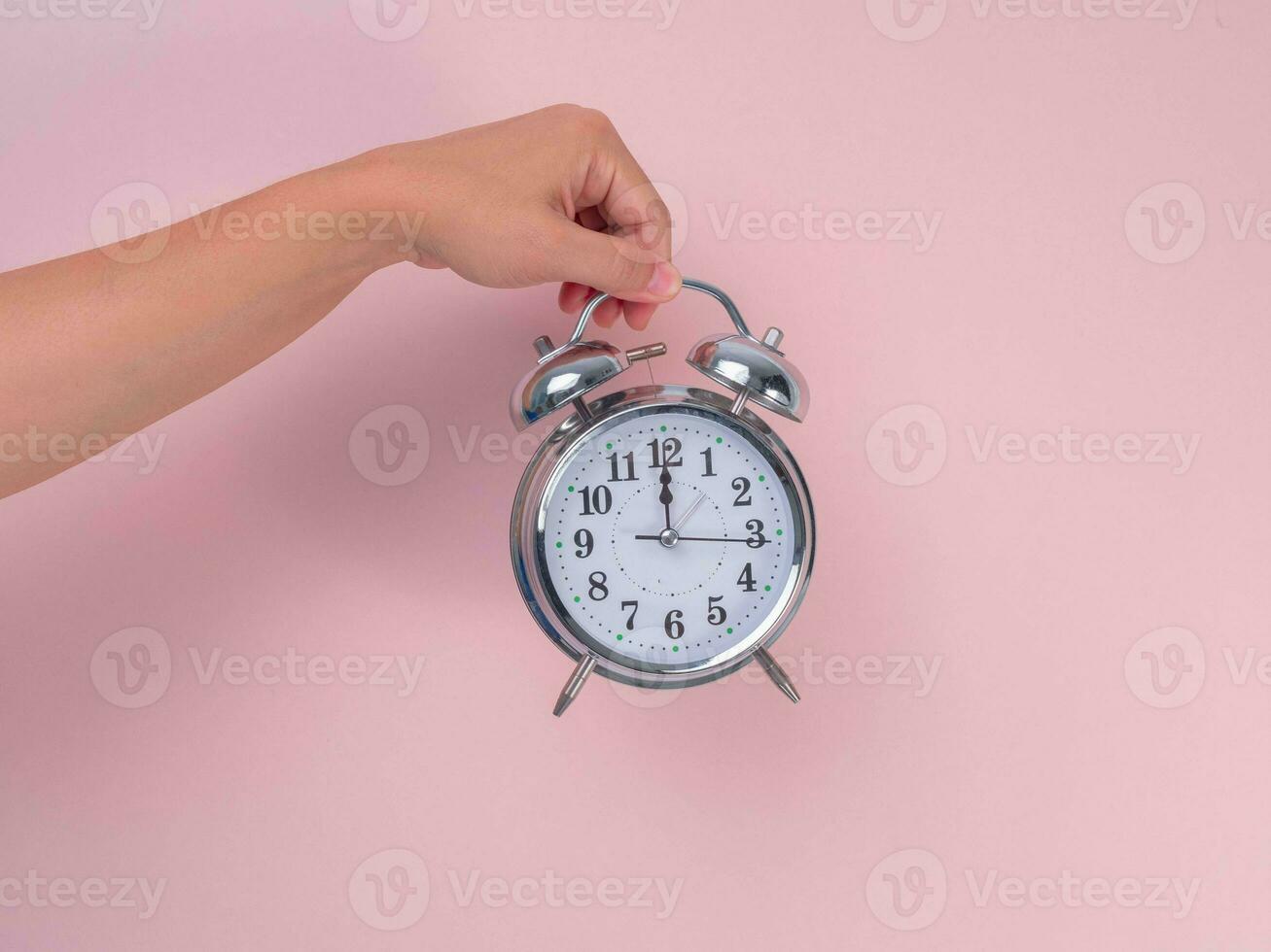 vrouw hand- Holding klassiek alarm klok Aan roze achtergrond. dichtbij omhoog van alarm klok in hand. foto
