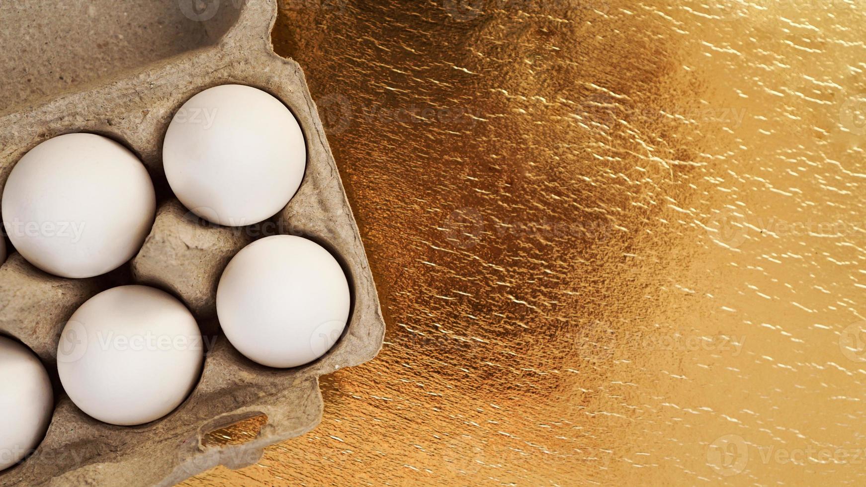 witte kippeneieren in een kartonnen bakje op een gouden achtergrond foto