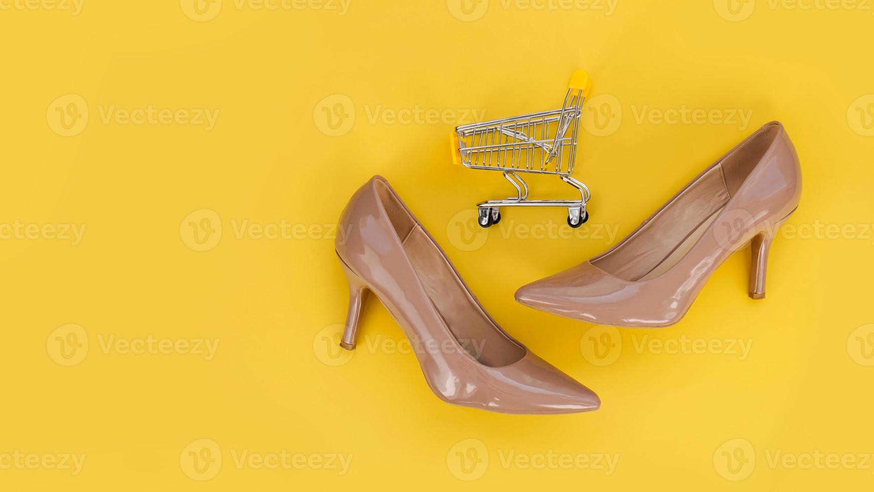 beige schoenen en een winkelwagentje op een gele achtergrond. foto