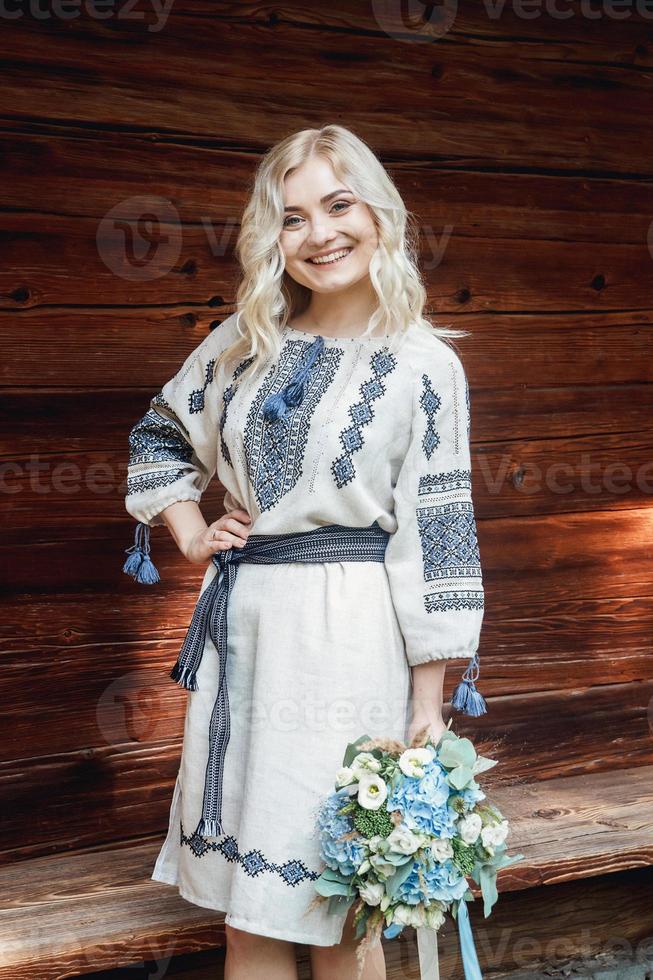 mooie vrouw in geborduurd shirt in de buurt van een houten huis foto