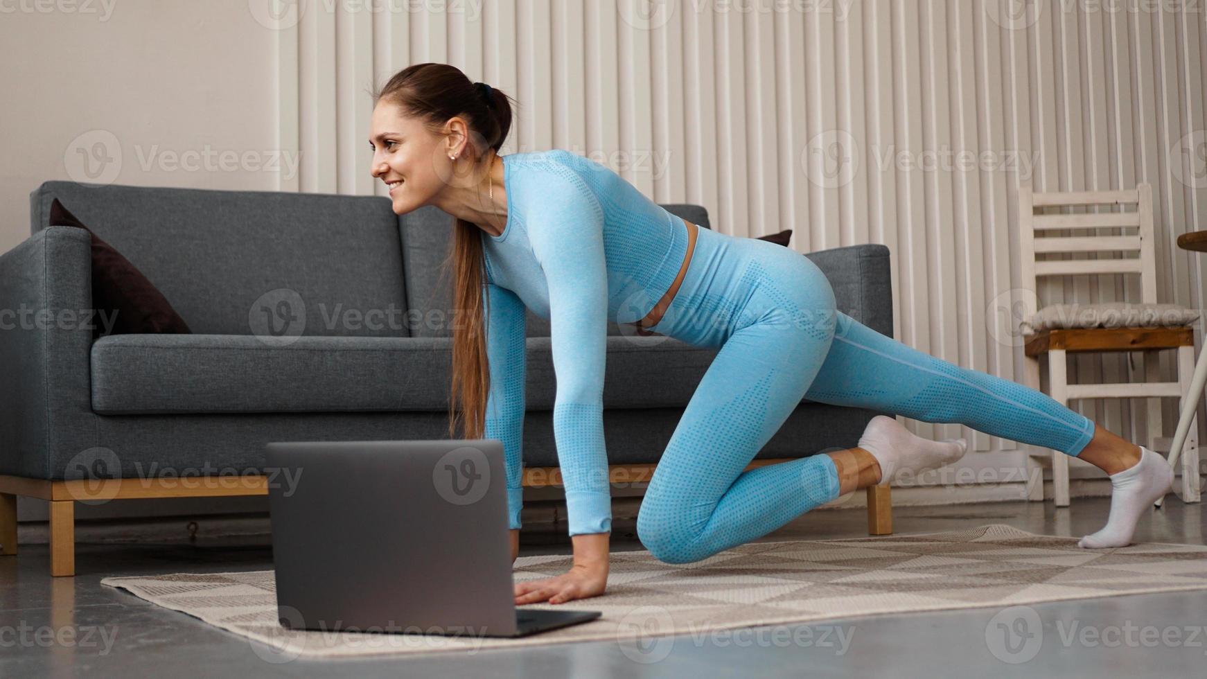 mooie jonge vrouw die thuis fitnessoefeningen doet met haar laptop foto