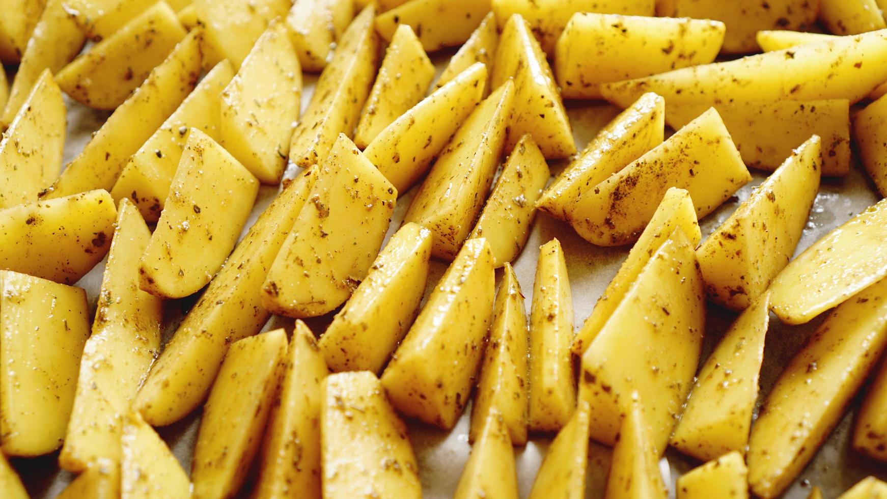 gesneden rauwe aardappelen op een bakplaat met kruiden foto