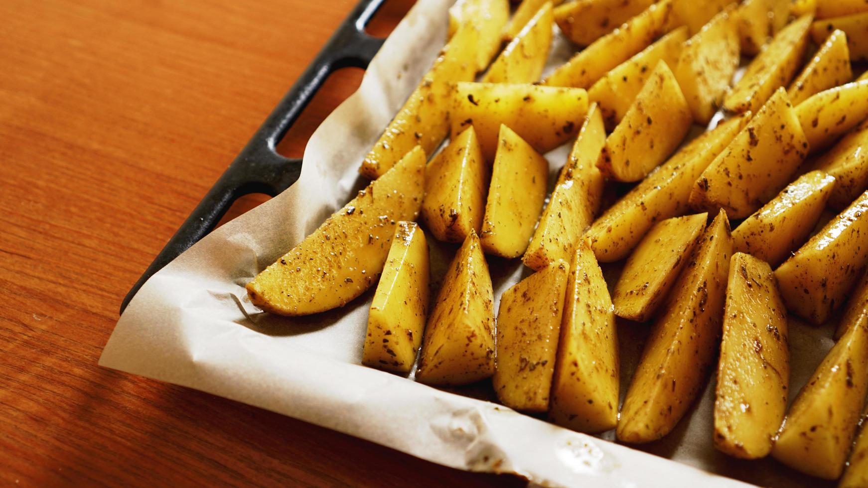 gesneden rauwe aardappelen op een bakplaat met kruiden foto