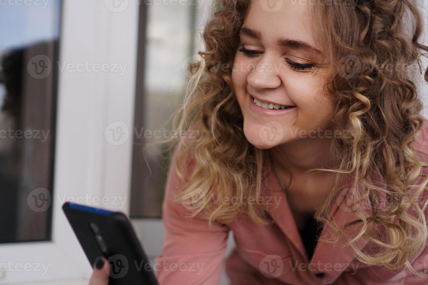 vrolijke prachtige jonge vrouw met krullend haar met smartphone foto