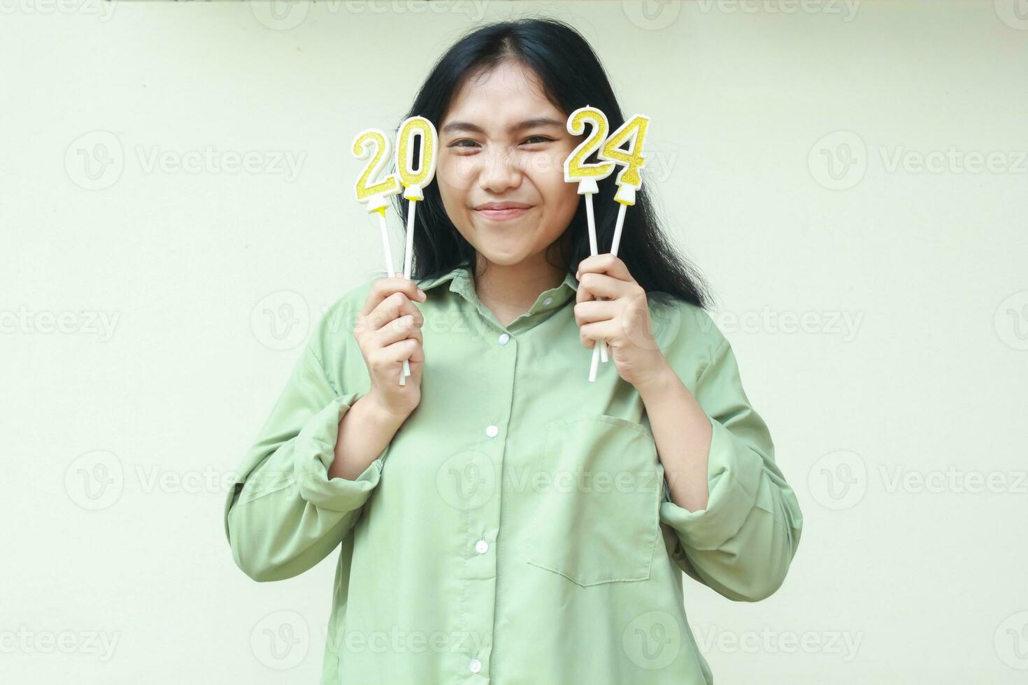 gelukkig Aziatisch jong vrouw Holding gouden kaarsen 2024 aantal en op zoek Bij camera met glimlachen gezicht slijtage Grean over- grootte overhemd vieren nieuw jaren vooravond geïsoleerd Aan wit achtergrond foto