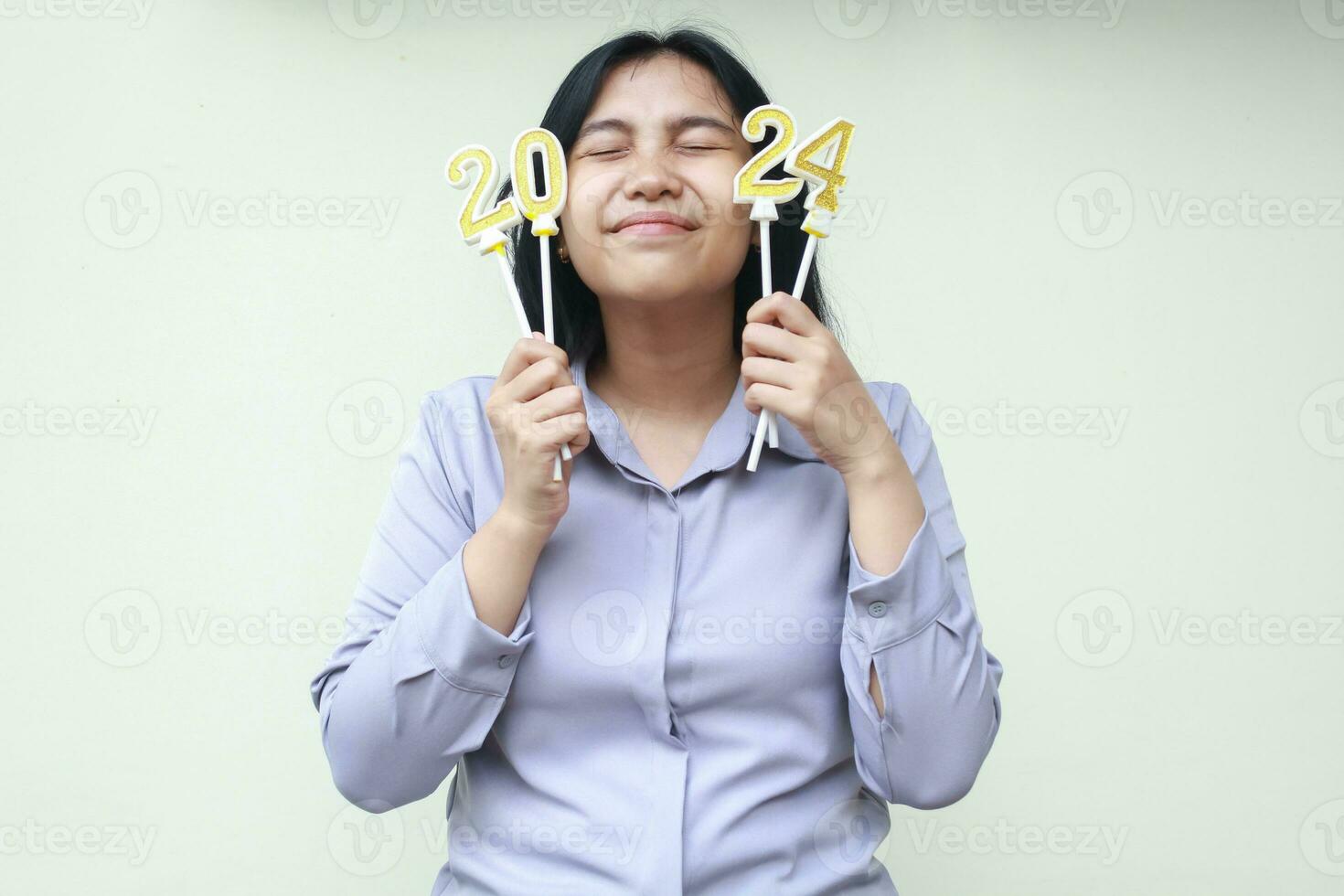 gelukkig Aziatisch jong vrouw glimlachen met ogen Gesloten en Holding kaarsen 2024 getallen naar vieren nieuw jaren vooravond met opwinding slijtage grijs formeel pak geïsoleerd Aan wit achtergrond foto