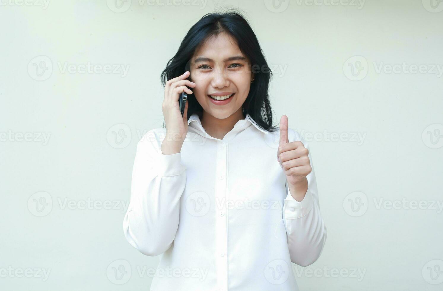 portret van geslaagd zelfverzekerd Aziatisch jong vrouw ondernemer sprekend Aan smartphone en op zoek Bij camera geven duimen omhoog gevoel tevreden van onderhoud vervelend wit formeel shirt, staand geïsoleerd foto