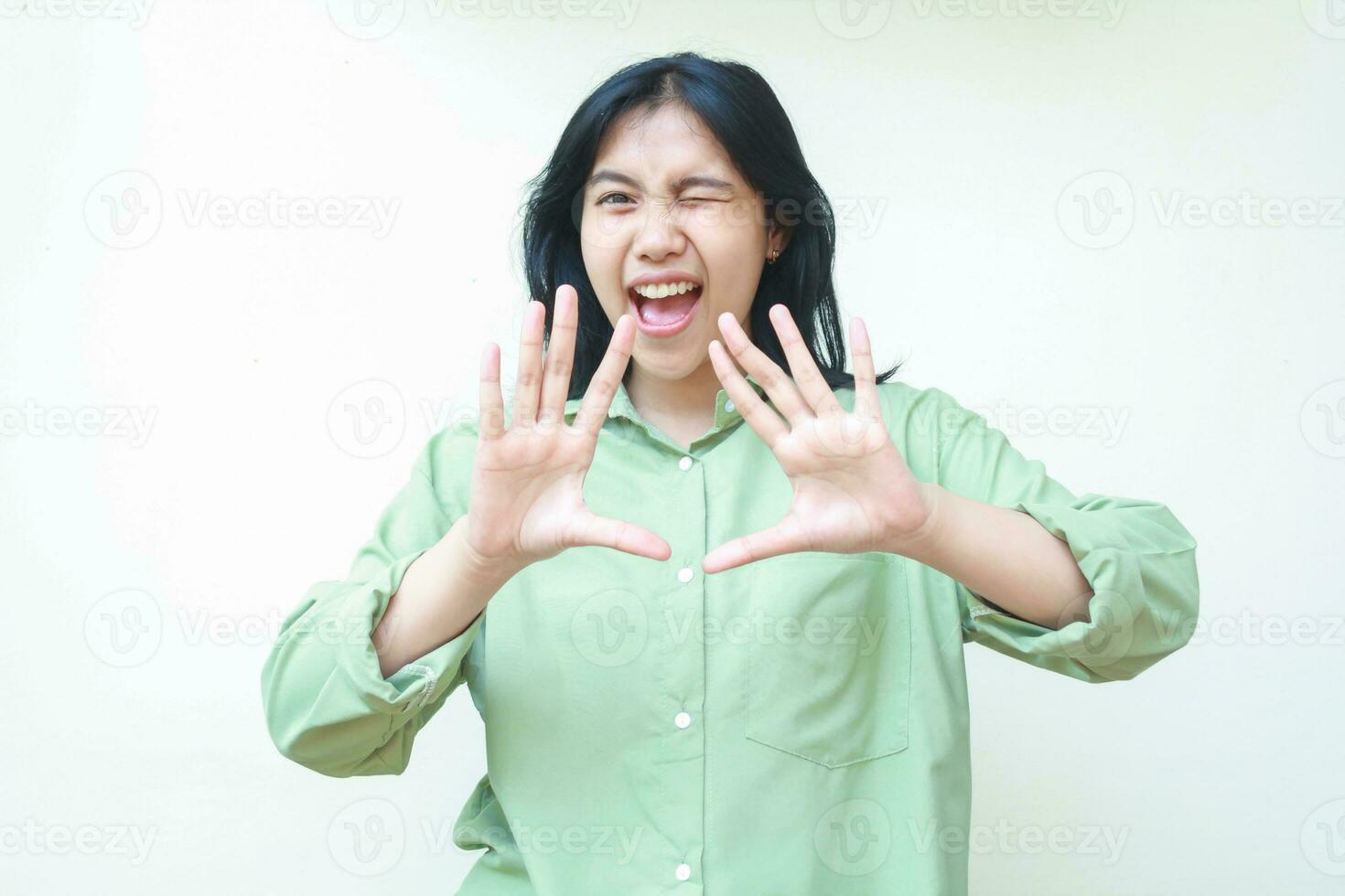 gelukkig Aziatisch vrouw verrast op zoek Bij camera met verhogen palmen tonen hou op gebaar, waarschuwing, flirten en knipperen oog, vervelend groen te groot overhemd geïsoleerd Aan wit achtergrond foto