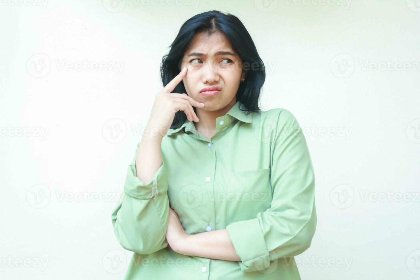 attent Aziatisch vrouw met donker haar- op zoek weg nieuwsgierig met vouwen armen en aanraken haar wang vervelend groen te groot shirt, geërgerd vrouw gevoel bang en bang geïsoleerd Aan wit foto