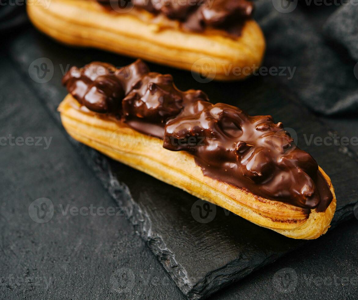 twee eclairs met donker chocola Aan zwart bord foto