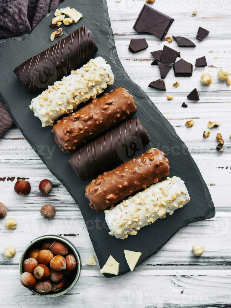 Frans toetje eclairs of profiteroles met verschillend chocola suikerglazuur Aan een zwart steen bord foto