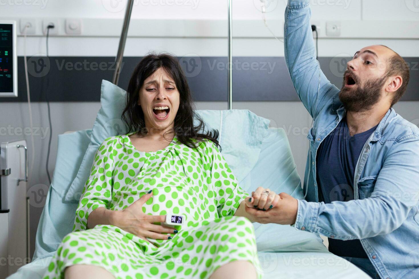 jong paar ervan uitgaand baby in ziekenhuis afdeling bed Bij gezondheidszorg faciliteit. vrouw met zwangerschap hebben pijnlijk weeën krijgen in arbeid terwijl man in paniek raken over bevalling. foto