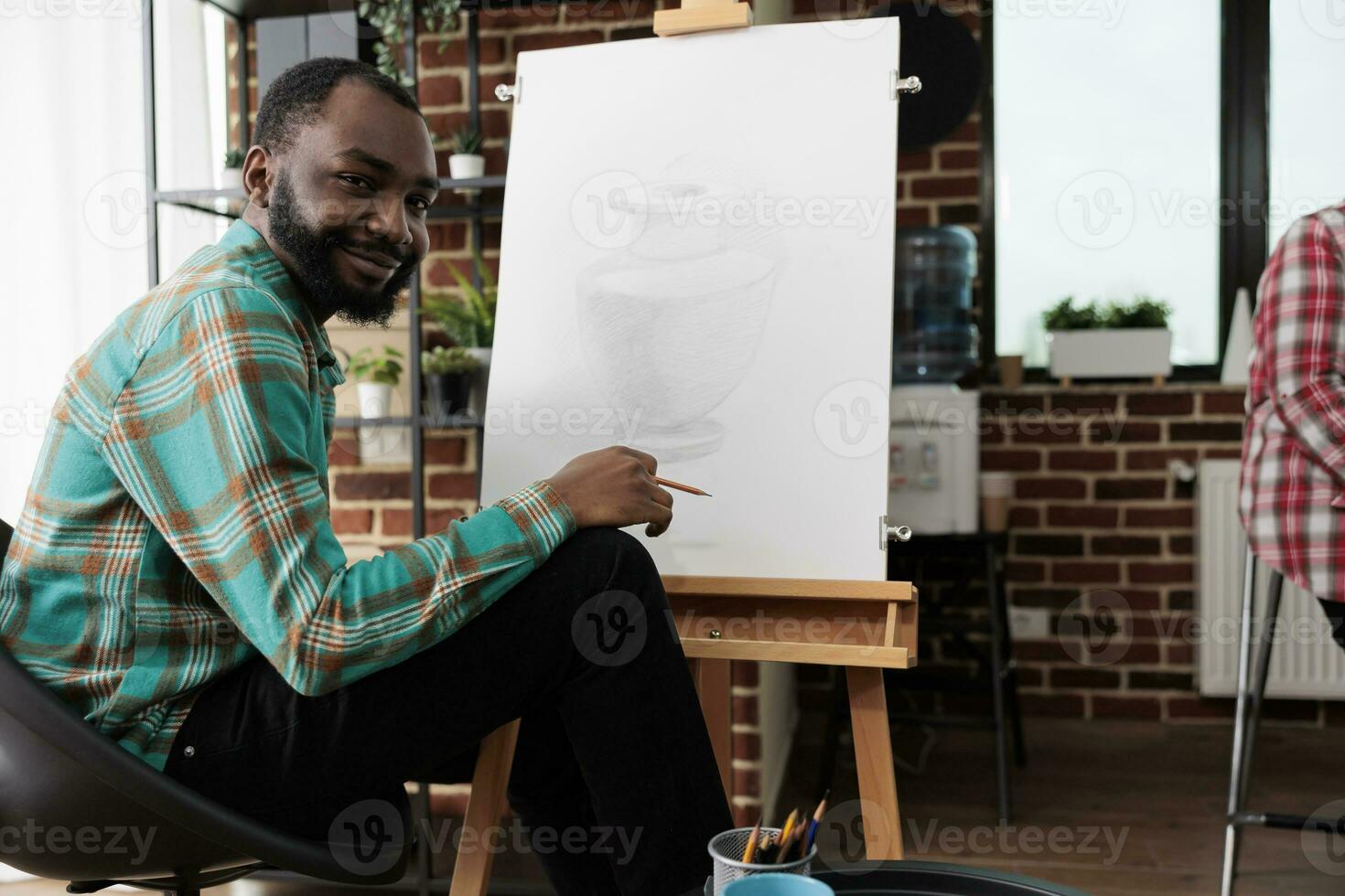 kunst activiteiten en welzijn. portret van gelukkig glimlachen Afrikaanse Amerikaans vent gedurende tekening les, jong zwart Mens zittend Bij ezel op zoek Bij camera, gevoel geïnspireerd gedurende schetsen klasse foto