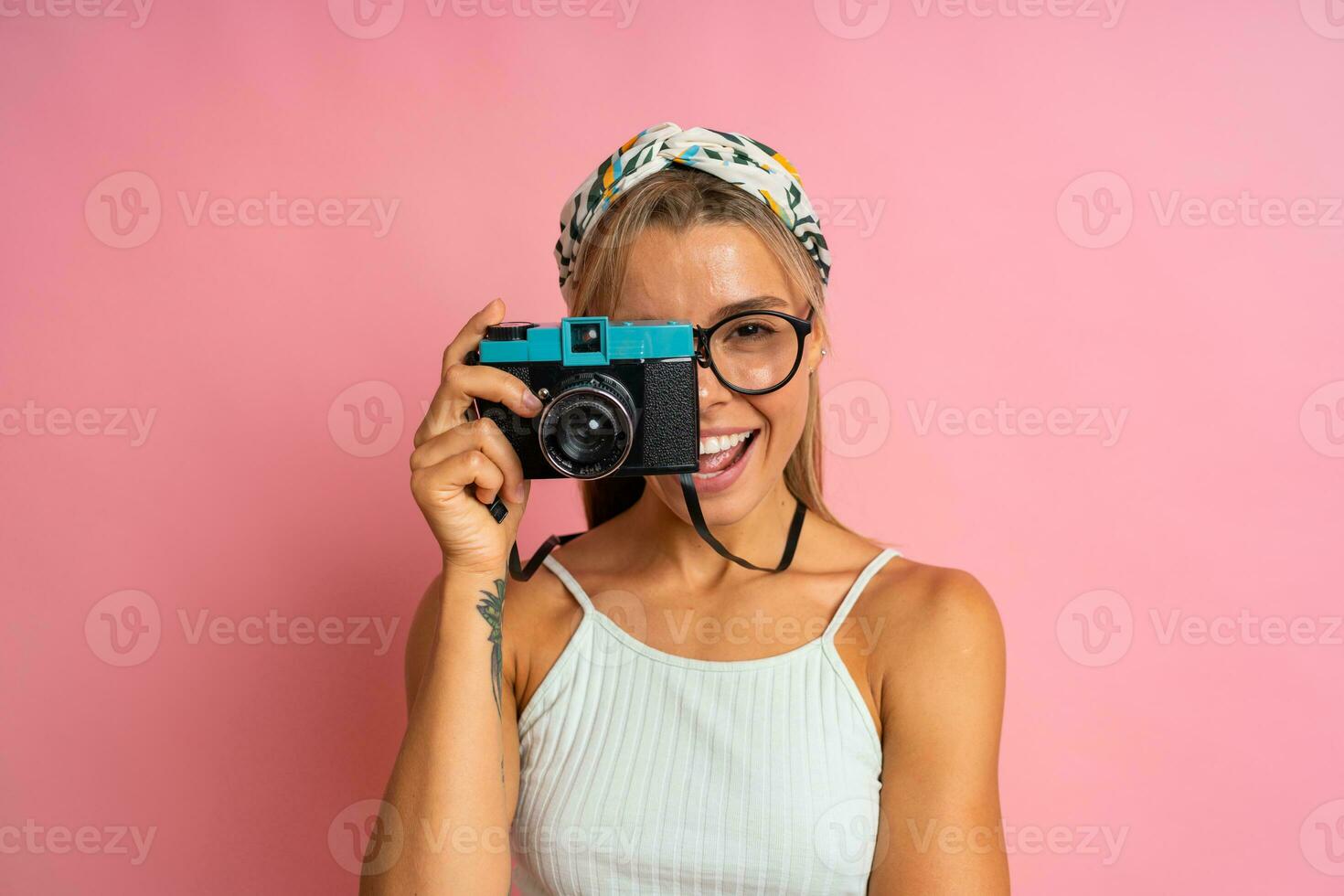 lachend blond vrouw Holding retro camera en poseren Aan roze achtergrond. reizen en zomer vakantie concept. foto